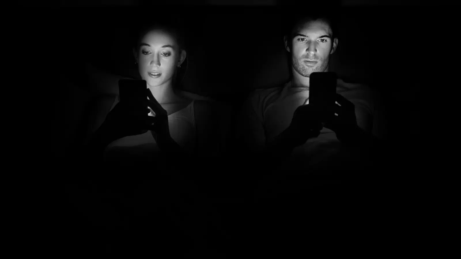 A couple in bed, faces lit by their phones in the dark